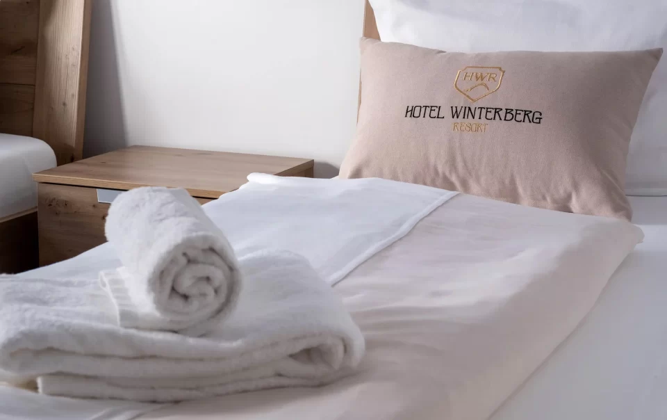 Gevouwen handdoeken en kussen met hotellogo op een gastenbed