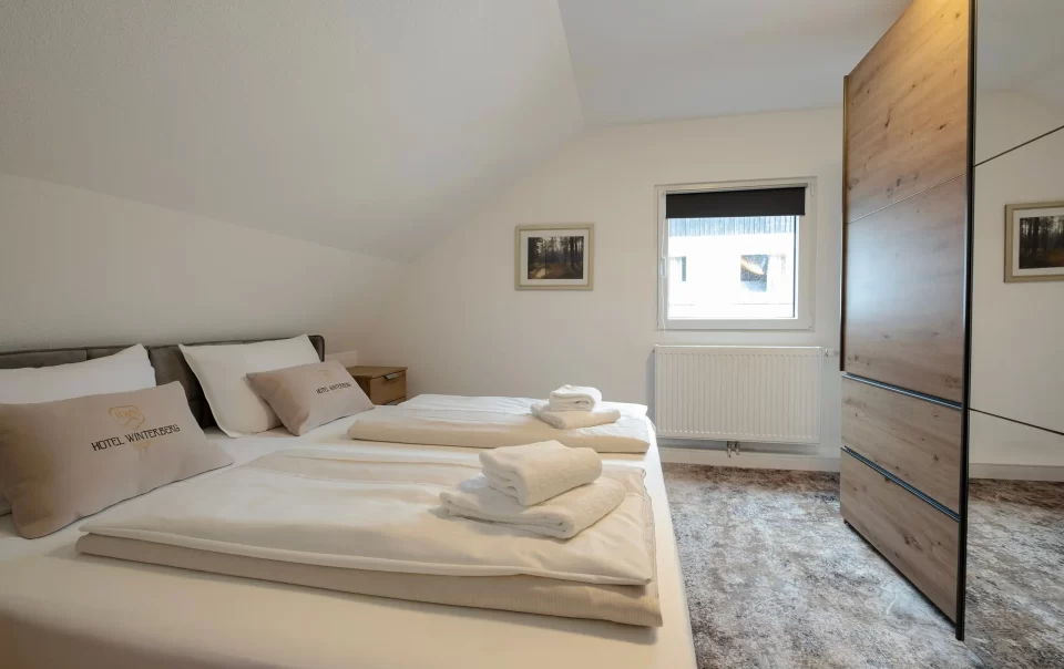 Doppelbett mit weißer Bettwäsche und gefalteten Handtüchern