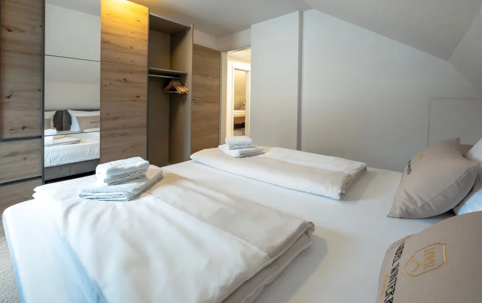 Doppelbett mit weißer Bettwäsche und gefalteten Handtüchern