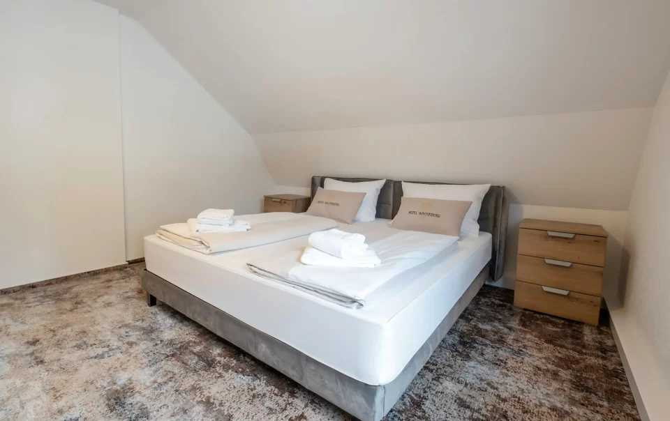 Doppelbett mit weißer Bettwäsche und gefalteten Handtüchern