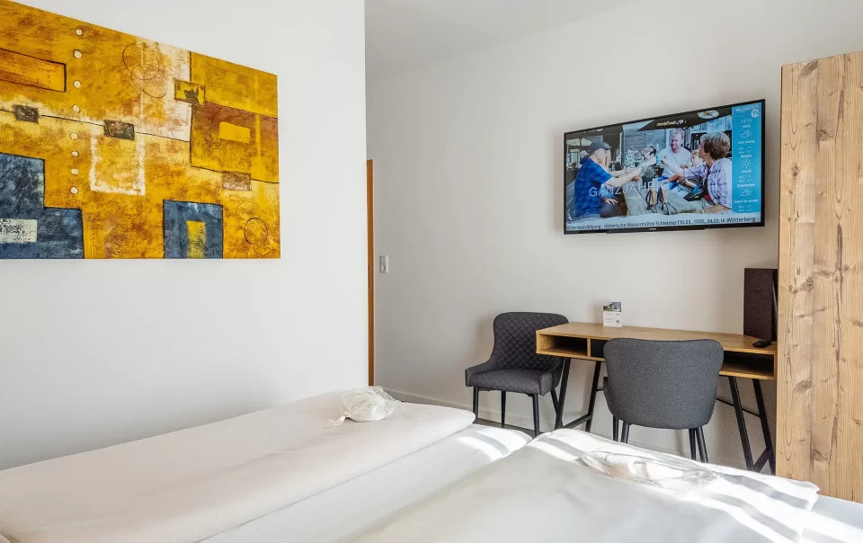 Guest bed with colourful artwork and television nearby