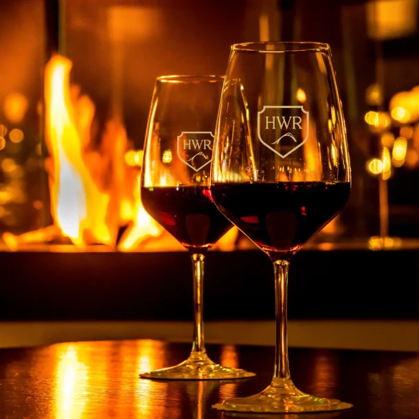 Red wine glasses beside a glowing fireplace