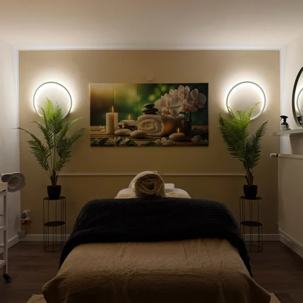 Spa treatment room with a massage bed, warm lights and plants