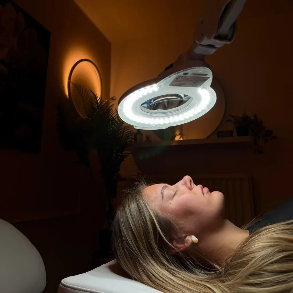 Guest reclining beneath an illuminated magnifying lamp in the spa at Hotel Winterberg Resort.