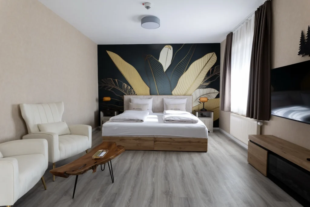 Wide room view with two beds, cream armchairs and a leaf-patterned wall